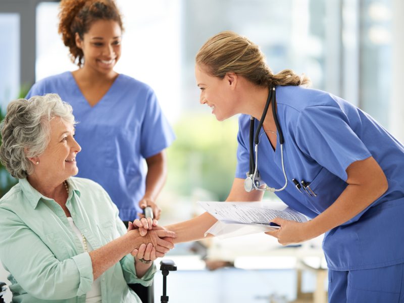 Shot of an attractive female nurse holding medical records while shaking hands with her wheelchair-bound senior patient in the hospital