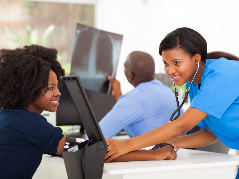 caring african young nurse checking patient's blood pressure in doctor's office