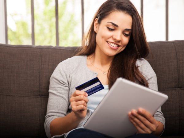 Cute young woman shopping online with her credit card and a tablet computer at home