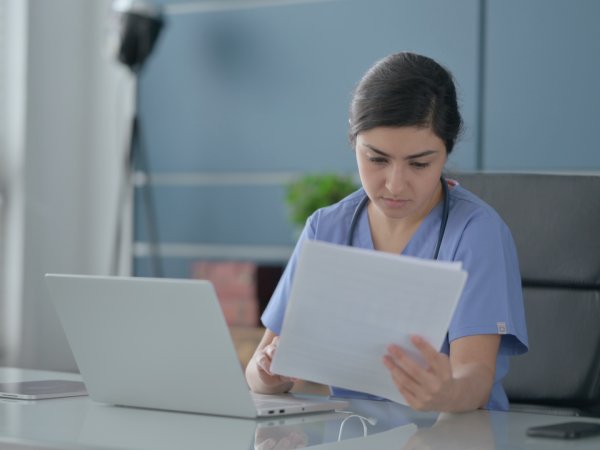Indian Female Doctor with Laptop Reading Documents in Office
