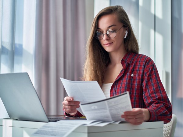 Modern young woman in glasses holds resume during online job searching