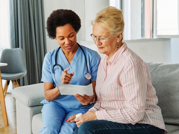 Doctor or nurse caregiver showing a prescrption drug bottle to senior woman at home or nursing home