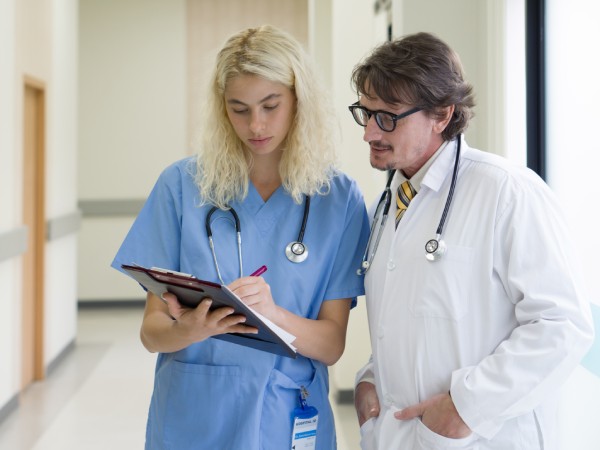 Médico caucásico de alto nivel discutiendo en el pasillo de un hospital con una enfermera.